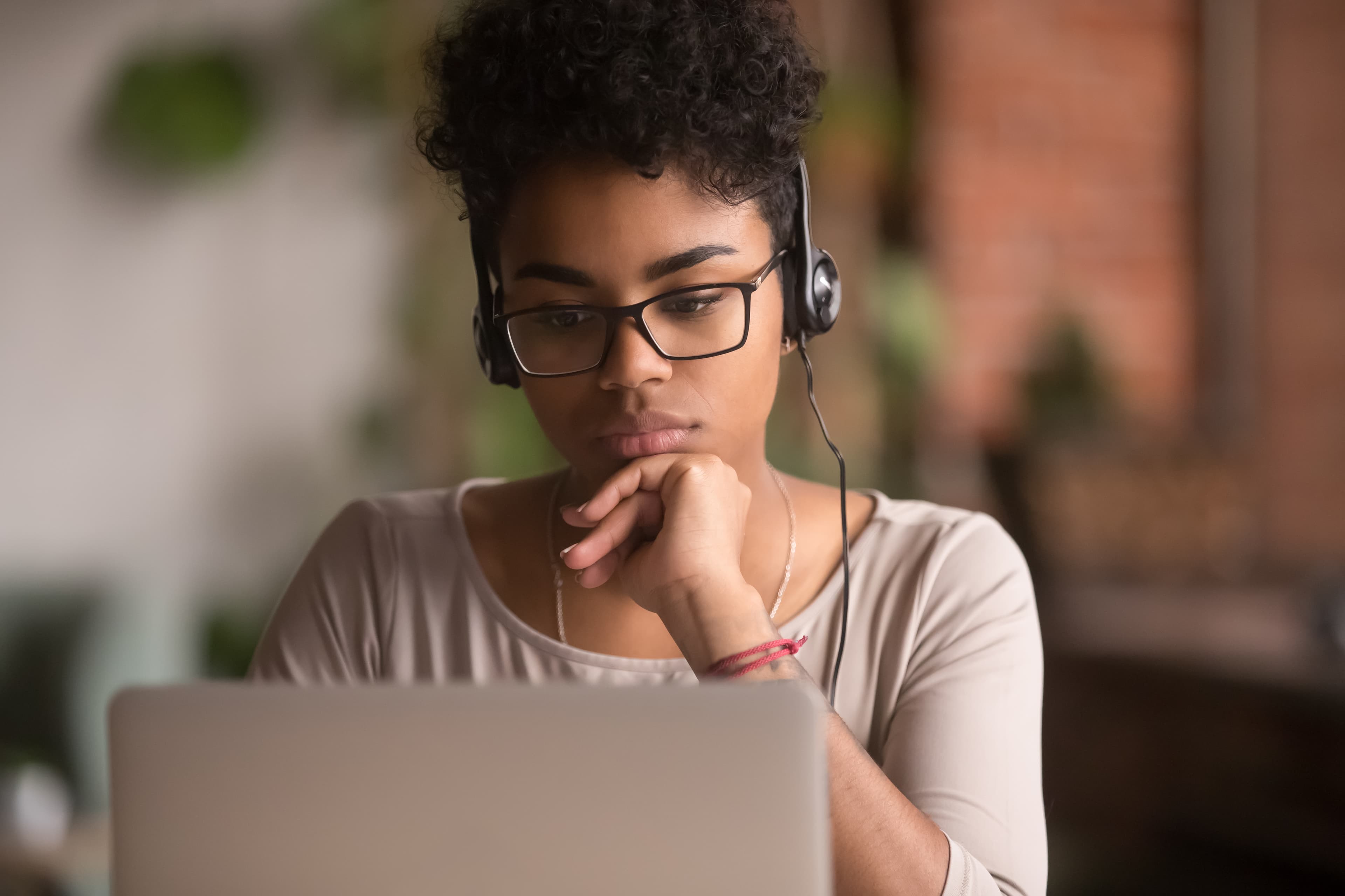 Woman wearing a headset and glasses focused on a laptop